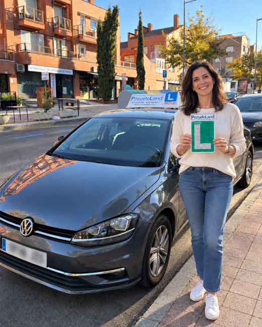 Mujer de unos 40 años posando con su placa de la L junto a un coche de prácticas de una autoescuela PozueloLand en Pozuelo de Alarcón, celebrando su nuevo carnet de conducir